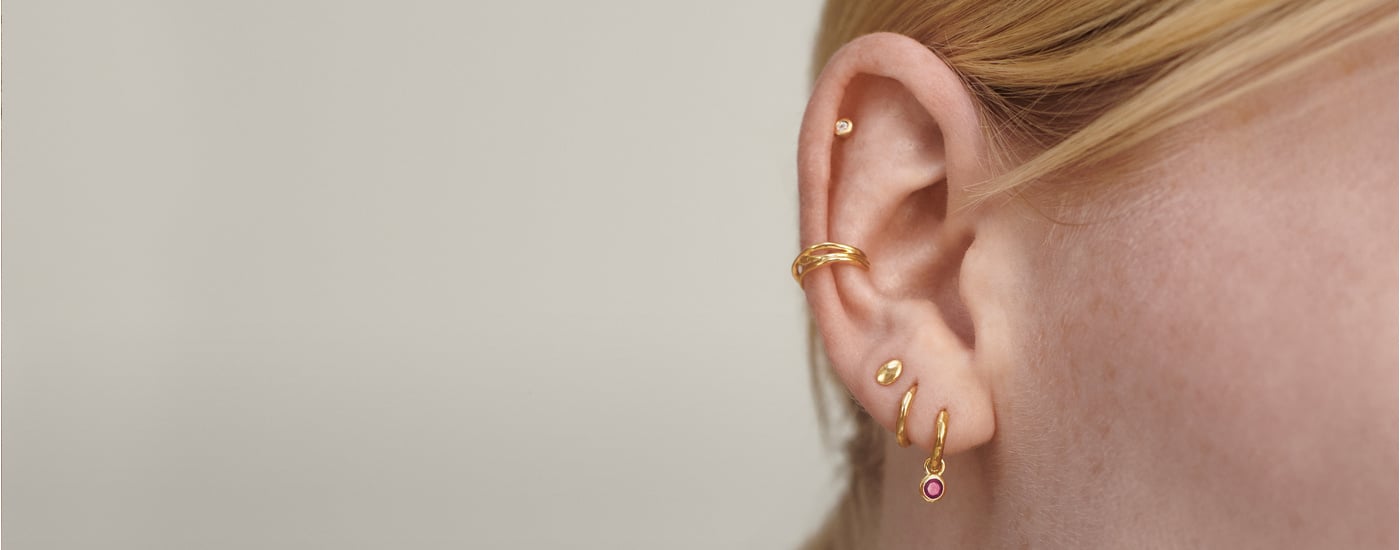 Model wearing gold studs and hoops, with diamonds and pink gemstones