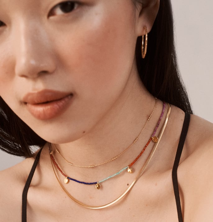 A model wearing textured medium hoops, and layered necklaces with colourful gemstones
