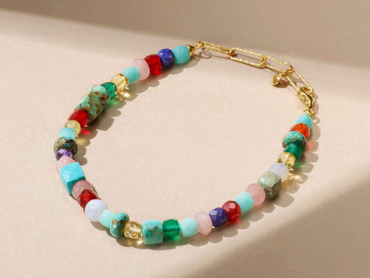 A gemstone bracelet of blue, green, pink, purple and red stones sits on a beige background.